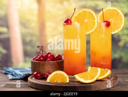 Tequila Sonnenaufgangscocktail mit Orangenscheibe und Kirsche auf einem rustikalen Holztisch mit ländlichem Hintergrund Stockfoto