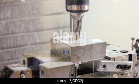 Waschen einer CNC-Bohrmaschine aus gesägtem Metall in Nahaufnahme. Wasserfluss auf den Bohrer und den Metallblock. Stockfoto