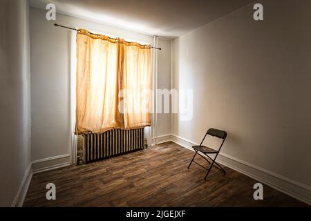 Vergilbter Vorhang in einem heruntergekommenen Zimmer mit einarmigtem Stuhl Stockfoto