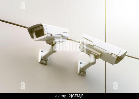Nahaufnahme von zwei CCTV-Kameras an einer weißen Wand auf der Straße. Stockfoto