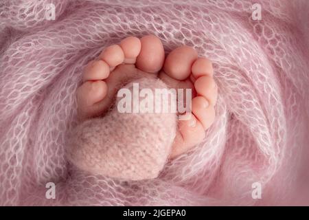 Gestricktes rosa Herz in die Beine eines Babys. Weicher Fuß eines Neugeborenen. Nahaufnahme von Zehen, Fersen und Füßen eines Neugeborenen. Stockfoto