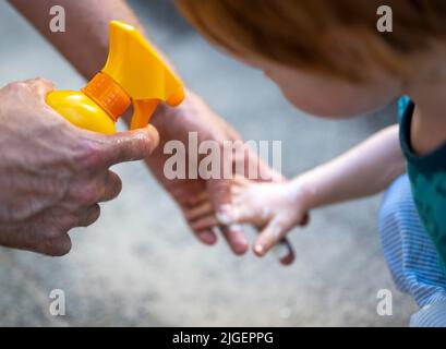 Berlin, Deutschland. 04.. Juli 2022. Ein Mann legt Sonnencreme auf die Hand seines Kindes. Quelle: Monika Skolimowska/dpa/Alamy Live News Stockfoto