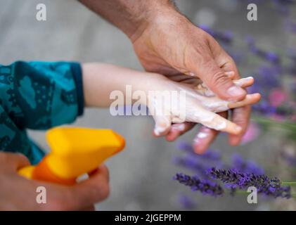 Berlin, Deutschland. 04.. Juli 2022. Ein Mann legt Sonnencreme auf die Hand seines Kindes. Quelle: Monika Skolimowska/dpa/Alamy Live News Stockfoto