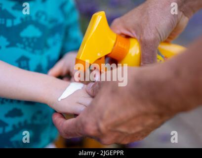 Berlin, Deutschland. 04.. Juli 2022. Ein Mann legt Sonnencreme auf die Hand seines Kindes. Quelle: Monika Skolimowska/dpa/Alamy Live News Stockfoto