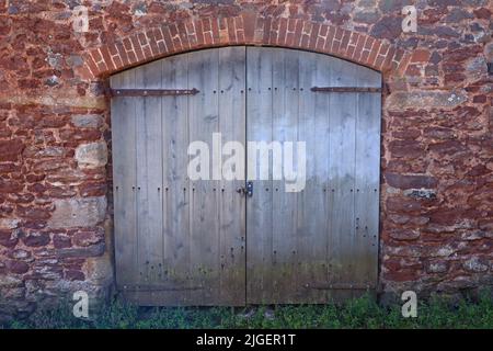 Alte braune Doppeltüren mit gewölbter Oberseite auf einer Scheune in Dunster in Somerset, England Stockfoto