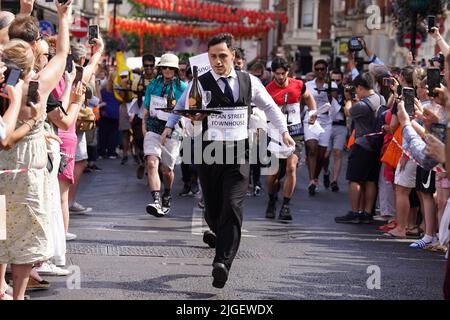 Die Menschen nehmen am Soho Waiter's Race im Soho Village Fete, Wardour Street, London, Teil. Eine Hundeschau, ein Spaghetti-Fressen-Wettbewerb und ein Kriegsschlepper der Polizei gegen die Feuerwehr sind alle Teil der Festivites auf dem Fete. Bilddatum: Sonntag, 10. Juli 2022. Stockfoto