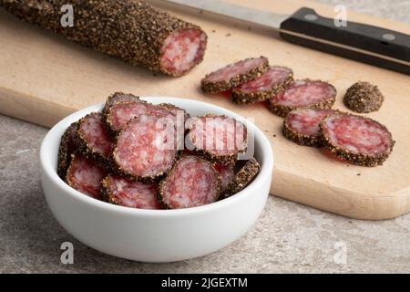 Traditionelle katalanische Wurst, Fuet und mit schwarzem Pfeffer überzogene Scheiben auf einem Schneidebrett aus nächster Nähe Stockfoto