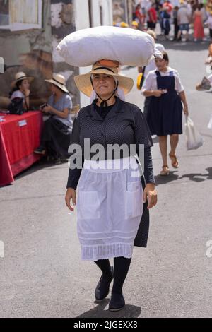 Chirche, Teneriffa, 10. Juli 2022. Eine Frau trägt einen Sack Waren auf ihrem Kopf, als sie die Straße entlang geht. Die Dorfbewohner feiern den Día de tradiciones, den Tag der Traditionen in dem kleinen Bergdorf, wo sie Szenen aus dem ländlichen Lebensstil ihrer Vorfahren im Jahr 1940s umspielen Stockfoto