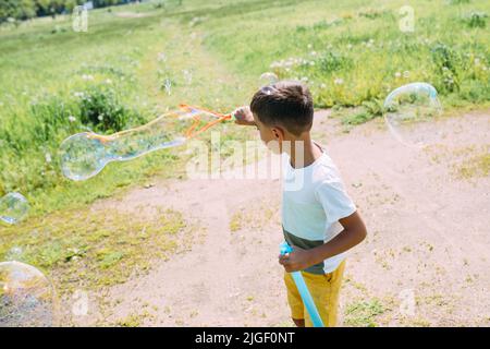 Vorschulkinder blasen an einem sonnigen Tag große Seifenblasen auf einem Feld Stockfoto