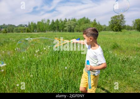 Vorschulkinder blasen an einem sonnigen Tag große Seifenblasen auf einem Feld Stockfoto