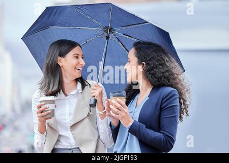 Regen oder Sonnenschein, gut immer noch erfolgreich. Porträt zweier junger Geschäftsfrauen, die Kaffee trinken, während sie unter einem Regenschirm in der Stadt stehen. Stockfoto