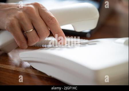 Nahaufnahme der weiblichen Telefonnummer mit dem weißen Festnetztelefon. Stockfoto