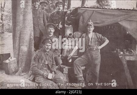 „Britischer Soldat kocht an der Somme mit Trophäen“: Foto mit britischen Soldaten an einer provisorischen Küche in einem Wald an der Westfront. Einer trägt einen deutschen Pickelhaube-Helm (ein anderer Soldat hält einen deutschen Helm im Hintergrund). Blechbecher, Mistdosen und Benzinkanister sind auch auf dem Bild zu sehen, das als Postkarte veröffentlicht wurde, die für den Blinded Soldiers Children Fund verkauft werden soll Stockfoto