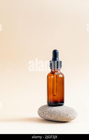 Bernsteinfarbene Tropfflasche mit schwarzem Deckel auf einem Podium auf Steinen. Hautpflegeprodukte, Naturkosmetik. Schönheitskonzept für die Gesichts- und Körperpflege Stockfoto