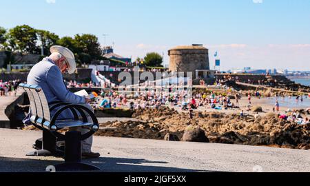 Ein Mann liest am Sonntag bei gutem Wetter am Seapoint Beach in South Dublin ein Buch von sich selbst, wie Eireann prognostizierte, dass die warmen und trockenen Tage mit den höchsten Temperaturen auf 25 Grad anstiegen. Bilddatum: Sonntag, 10. Juli 2022. Stockfoto