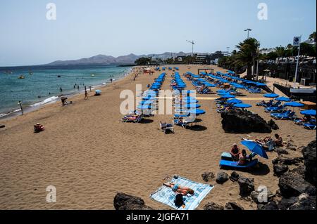 Touristen sonnen sich, schwimmen und entspannen sich am Playa Grande Beach in Puerto del Carmen, südöstlich auf der Vulkaninsel Lanzarote. Stockfoto