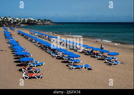 Touristen sonnen sich, schwimmen und entspannen sich am Playa Grande Beach in Puerto del Carmen, südöstlich auf der Vulkaninsel Lanzarote. Stockfoto