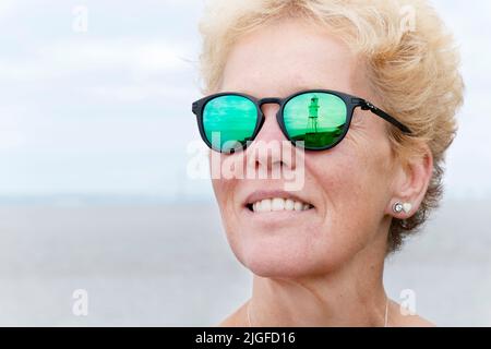 Ein Blick auf den Leuchtturm von Black Nore, Portishead, Großbritannien, spiegelt sich in der verschreibungspflichtigen Sonnenbrille einer Frau wider. Die Gläser sind in einem Oakley Pitchman R-Rahmen montiert Stockfoto