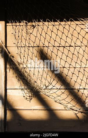 Fischernetz am Haus des Fischers. An der Holzwand hängendes Netzgewebe. Abstrakt Meer Leben Hintergrund. Stockfoto