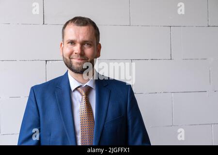 Ein kluger lächelnder, selbstbewusster arabischer Geschäftsmann vor dem Hintergrund einer weißen Stadtmauer. Porträt eines gutaussehenden reifen Geschäftsmannes in Anzug lächelnd Stockfoto