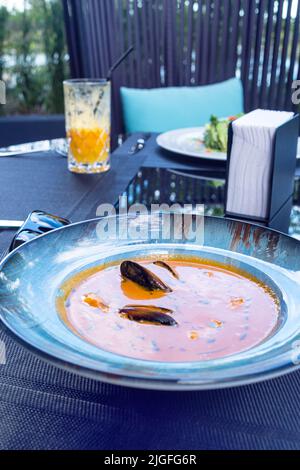 Köstliche Meeresfrüchte Tomatensoße mit Bouillabaisse Fischsuppe mit Garnelen, Muscheln und Fisch auf einem blauen Teller auf dem Tisch. Köstliches romantisches Abendessen in einer Fischruhe Stockfoto