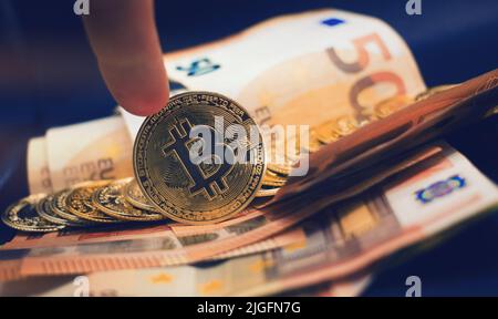 Handrollen einer Bitcoin mit einem Stapel von Münzen mit europäischen Banknoten als Hintergrund . Konzept der Kryptowährung . Stockfoto