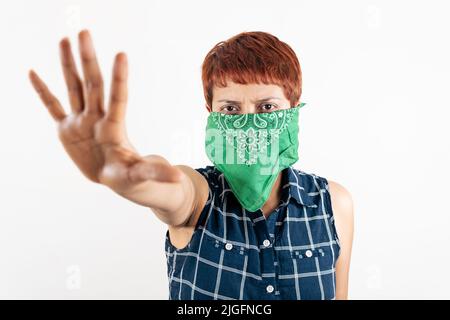 Eine lateinische Frau mittleren Alters bedeckt ihr Gesicht mit einem Schal und zeigt ihre Hand in einem Stoppschild Stockfoto