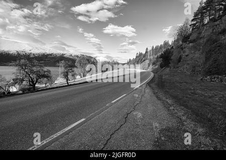 Eine Graustufenaufnahme einer Landstraße am Fjord in Norwegen mit Blick auf die Berge Stockfoto