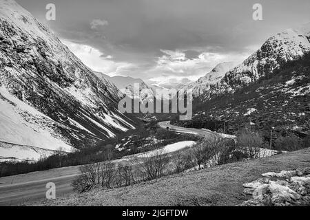 Eine Graustufenaufnahme einer kurvenreichen Straße durch verschneite Berge in Norwegen Stockfoto