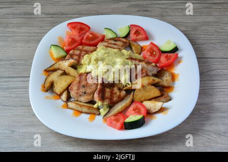 Schweinemedaillons mit Steinpilzen, frischem Gemüse und saurer Sauce in weißer Keramikplatte auf grauem Holzhintergrund serviert Stockfoto