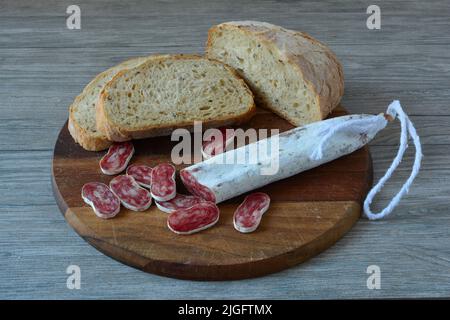 Sehr würzige spanische Wurst mit weißem Schimmel, in Scheiben geschnitten auf dunklem Holzbrett, mit etwas dunklem Brot, Seitenansicht Stockfoto