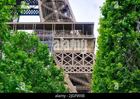 Paris, Frankreich - 26. Mai 2022: Nahaufnahme eines Teils des Eiffelturms, der durch Bäume gesehen wird und Namen französischer Wissenschaftler zeigt Stockfoto