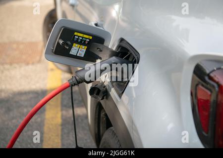 Das Elektroauto wird aufgeladen, es wird über das rote Kabel an die elektrische Steuereinheit angeschlossen, wo es Energie bezieht, und zwar auf einem eigenen Parkplatz. Stockfoto