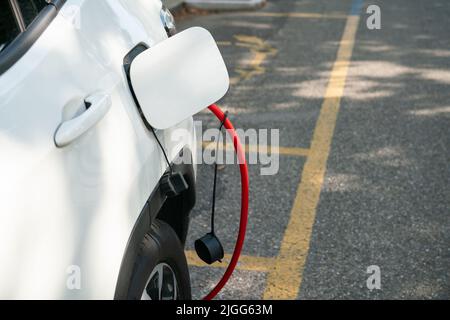 Das Elektroauto wird aufgeladen, es wird über das rote Kabel an die elektrische Steuereinheit angeschlossen, wo es Energie bezieht, und zwar auf einem eigenen Parkplatz. Stockfoto