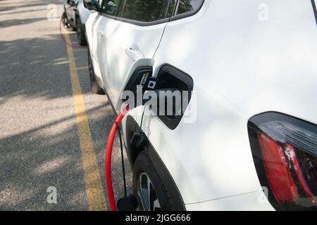 Auto: Elektroauto wird aufgeladen, verbunden mit dem gelben Kabel an die elektrische Steuereinheit, wo es Energie zieht, auf einem Parkplatz dedicat Stockfoto