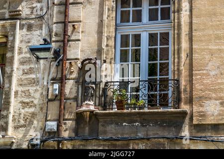 Eine kleine Madonna-Figur steht in einer Wandnische neben einem Balkon mit schmiedeeisernem Geländer in der Altstadt von Avignon, Frankreich. Solche Nischenstatuen an Fassaden sind typisch für die ehemalige Stadt der Päpste, die sich unter Marias Schutz sah. Stockfoto