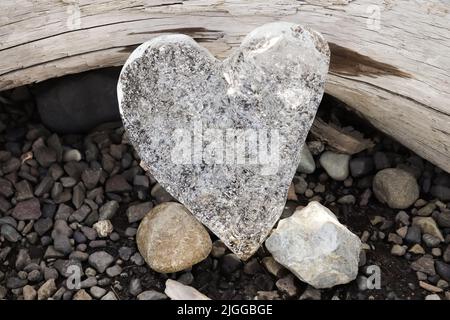 Ein Herz aus Eis, das sich gegen einen Baumstamm schief Stockfoto