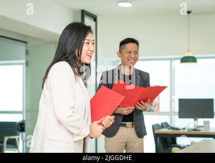 Geschäftsführerin, die eine Akte hält, während sie spricht und lächelt, Seitenansicht. Office-Schulung oder Briefing-Konzept. Stockfoto