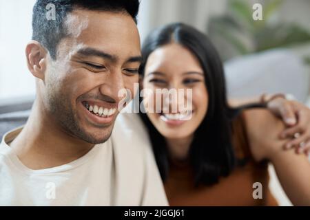 Ich lebe, um diesen Mann lächeln zu sehen. Ein junges Paar sitzt zusammen in ihrem Wohnzimmer zu Hause und verbindet. Stockfoto
