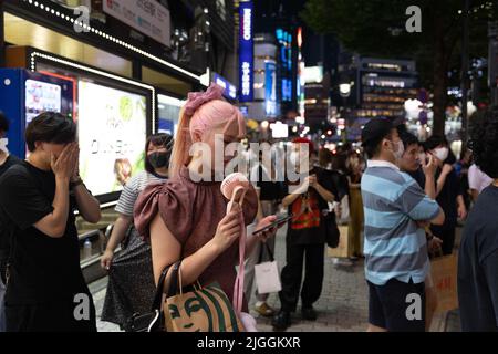 Frau ohne Gesichtsmaske wartet an einer Ampel in der Nähe des Bahnhofs Shibuya im Zentrum von Tokio. Am 30. Juni 2022 kündigte der japanische Gesundheits-, Arbeits- und Sozialminister Shigeyuki Goto die überarbeitete Position der Regierung zum Maskentragen an: „Selbst wenn Sie draußen an anderen Menschen vorbeikommen, wie zum Beispiel beim Gehen zur Arbeit, ist es nicht notwendig, eine Gesichtsmaske zu tragen, solange wenig oder gar keine Gespräche geführt werden.“ Grundsätzlich gesagt, dass das Tragen einer Gesichtsmaske draußen nicht mehr empfohlen wird. Stockfoto