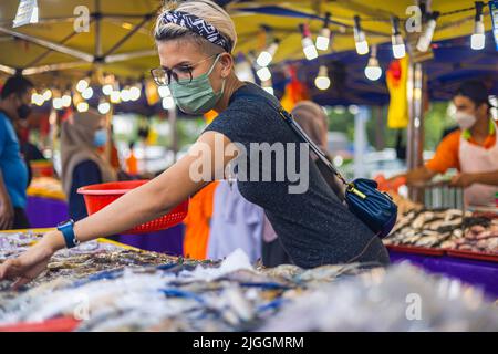 Kuala Lumpur, Malaysia - 21. Juni 2022: Junge asiatische Mädchen auf einem Frischmarkt oder Straßenmarkt in Kuala Lumpur, Malaysia, wählen Meeresfrüchte aus einem Fischhändler Stockfoto