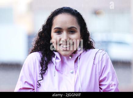 Regen hält sie nicht davon ab, herauszukommen. Eine junge Frau steht im Regen. Stockfoto