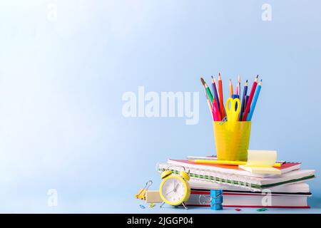 Viele verschiedene Schulen, Bürobedarf und Schreibwaren. Zurück zum Schulkonzept. Notizbuch, Buch, Stift, Bleistift, Schere, Wecker, Uhr, Aufkleber stehen auf einem Holztisch auf grünem Hintergrund. Stockfoto