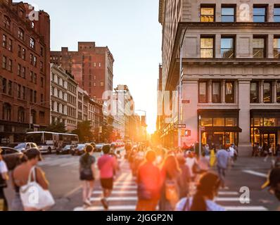 Menschen, die durch die geschäftige Kreuzung an der 5. Avenue und 23. Street in New York City gehen, mit Sonnenlicht im Hintergrund Stockfoto