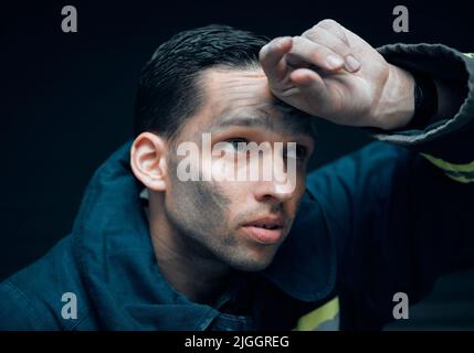 Es ist ein riskantes Geschäft. Studioaufnahme eines hübschen jungen männlichen Feuerwehrmundes, der vor schwarzem Hintergrund nachdenklich aussieht. Stockfoto