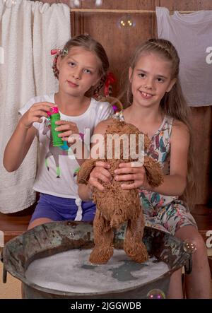 Kleine Freundinnen. Nette glückliche Mädchen baden Teddybären, blasen Blasen. Stockfoto