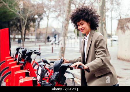 Lächelnde Frau, die ein Fahrrad von der Mietstation nimmt Stockfoto