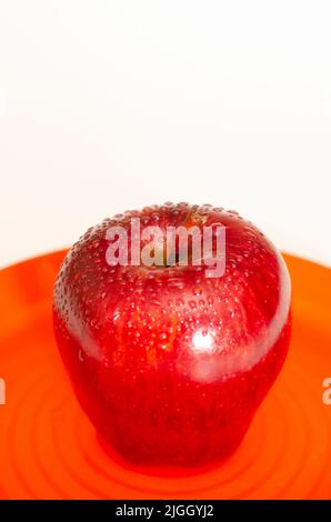 Frischer roter Apfel in orangefarbener Platte auf weißem Hintergrund Stockfoto