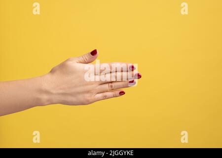 Nahaufnahme Profil Seitenansicht der Frau zeigt den Handrücken, schöne weiche Haut der weiblichen Hand, Handschlag. Innenaufnahme des Studios isoliert auf gelbem Hintergrund. Stockfoto