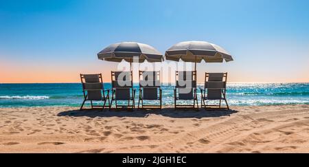 Liegestühle mit Sonnenschirm an einem schönen Sommertag. Stockfoto